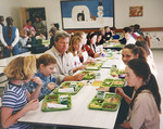 Max Baucus eating with children in school cafeteria by Creator unknown